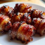 Close-up of several sticky, glazed Apple Butter Bacon Wrapped Smokies piled on a white plate.