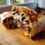 Close-up of a grilled BBQ Brisket Burritos cut in half, showing shredded brisket, rice, black beans, and melted cheese.