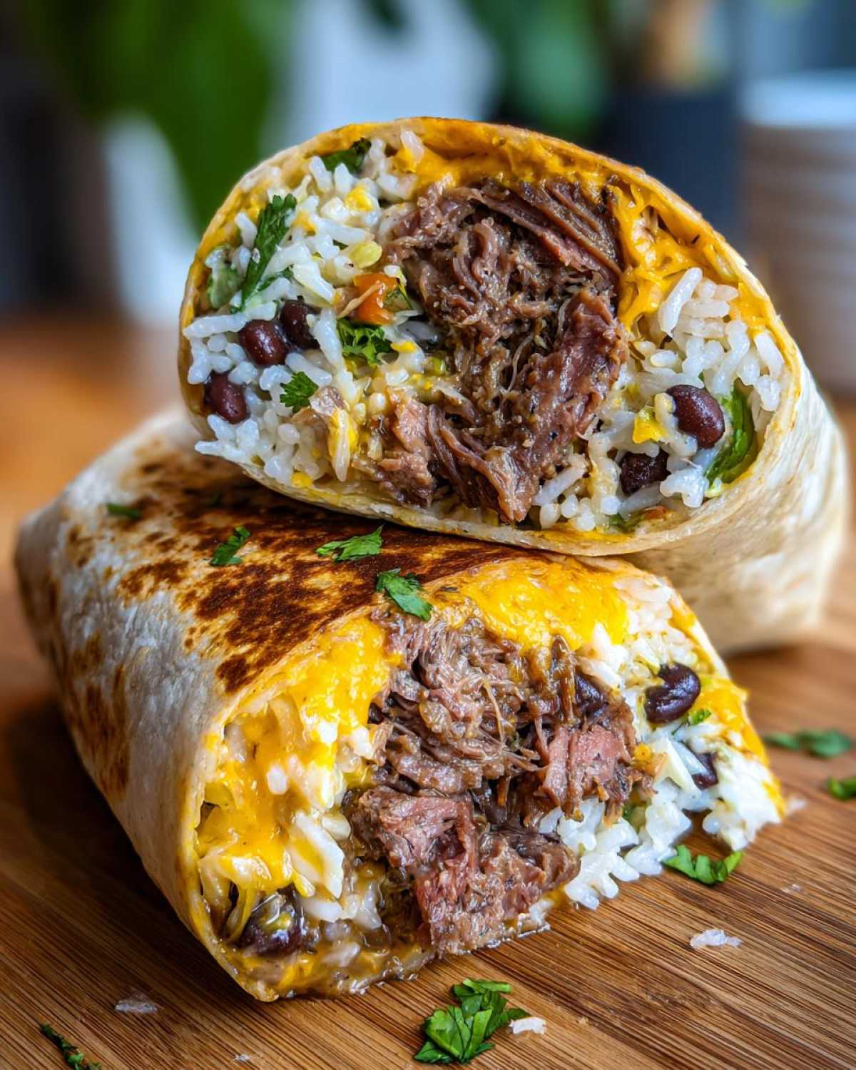A close-up of two halves of a BBQ Brisket Burritos stacked, showing shredded brisket, rice, black beans, and melted cheese.