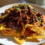 A close-up of loaded BBQ Jackfruit Nachos piled high with dark, saucy jackfruit and topped with fresh cilantro.
