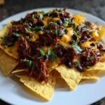 A plate of loaded BBQ Jackfruit Nachos topped with melted vegan cheese, black beans, and fresh cilantro.
