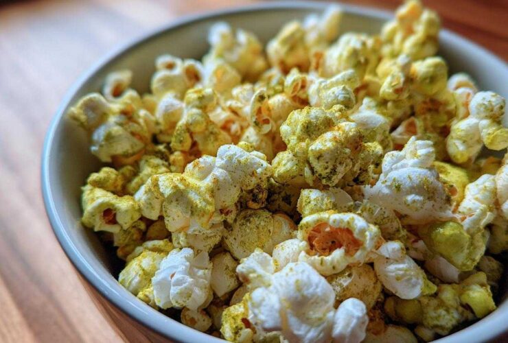 Close-up of a bowl filled with fluffy popcorn heavily coated in green and yellow Dill Pickle Seasoned Popcorn powder.