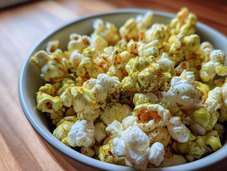 Close-up of a bowl filled with fluffy popcorn heavily coated in green and yellow Dill Pickle Seasoned Popcorn powder.
