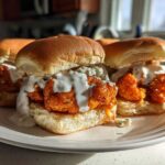 A plate holding several Buffalo Cauliflower Sliders topped generously with creamy blue cheese dressing.