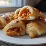 Golden baked Buffalo Chicken Pigs in a Blanket, one cut open to show the shredded spicy filling.