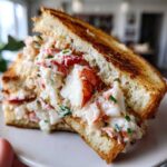 Close-up of a Butter-Poached Lobster Tail Sandwiches, showing chunks of white and red lobster meat mixed with creamy dressing and chives on toasted bread.