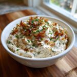A white bowl filled with creamy Caramelized Onion Neiman Marcus Dip, topped with crispy onions and fresh chives.