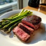 A perfectly seared Cast Iron Filet Mignon, sliced to show a medium-rare center, served alongside bright green asparagus spears.