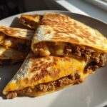 Four wedges of golden-brown Cheeseburger Quesadillas filled with seasoned ground beef and melted cheddar cheese, served on a white plate.
