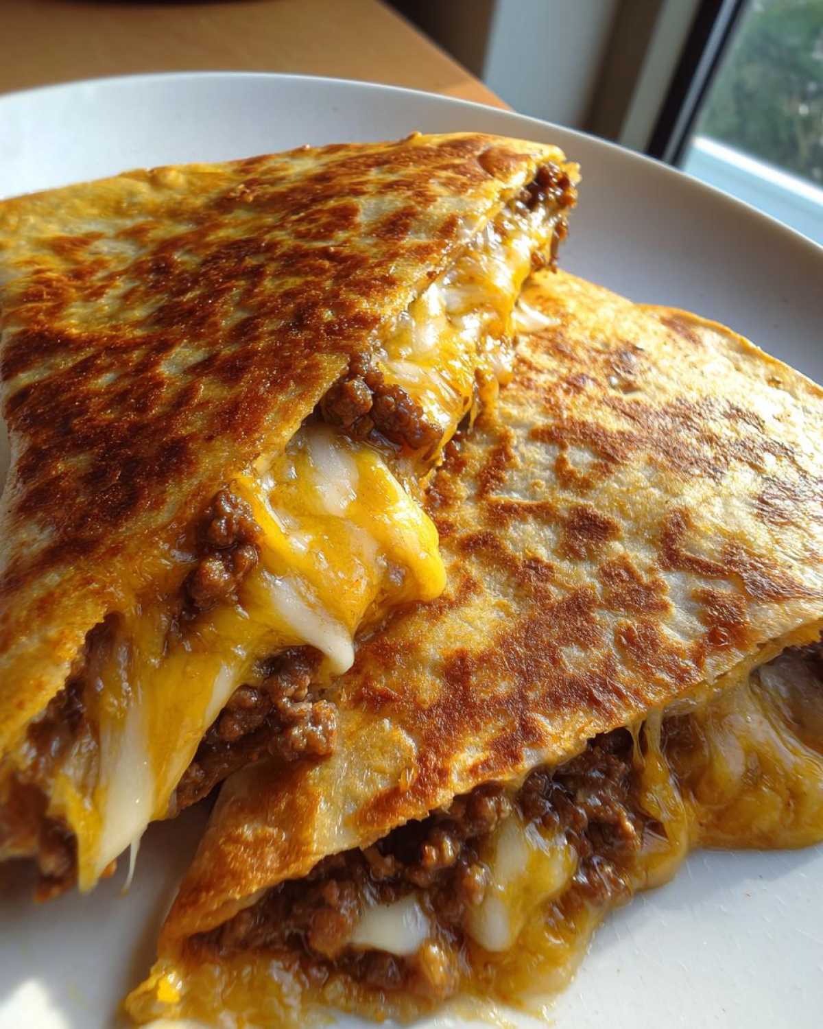 Close-up of two halves of Cheeseburger Quesadillas with Secret Sauce oozing melted cheese and seasoned ground beef.
