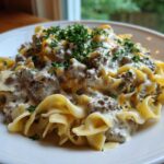 A close-up of Cheesy Ground Beef Stroganoff served over wide egg noodles and topped with fresh parsley.
