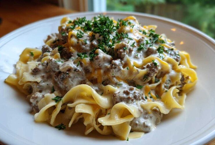 A close-up of Cheesy Ground Beef Stroganoff served over wide egg noodles and topped with fresh parsley.