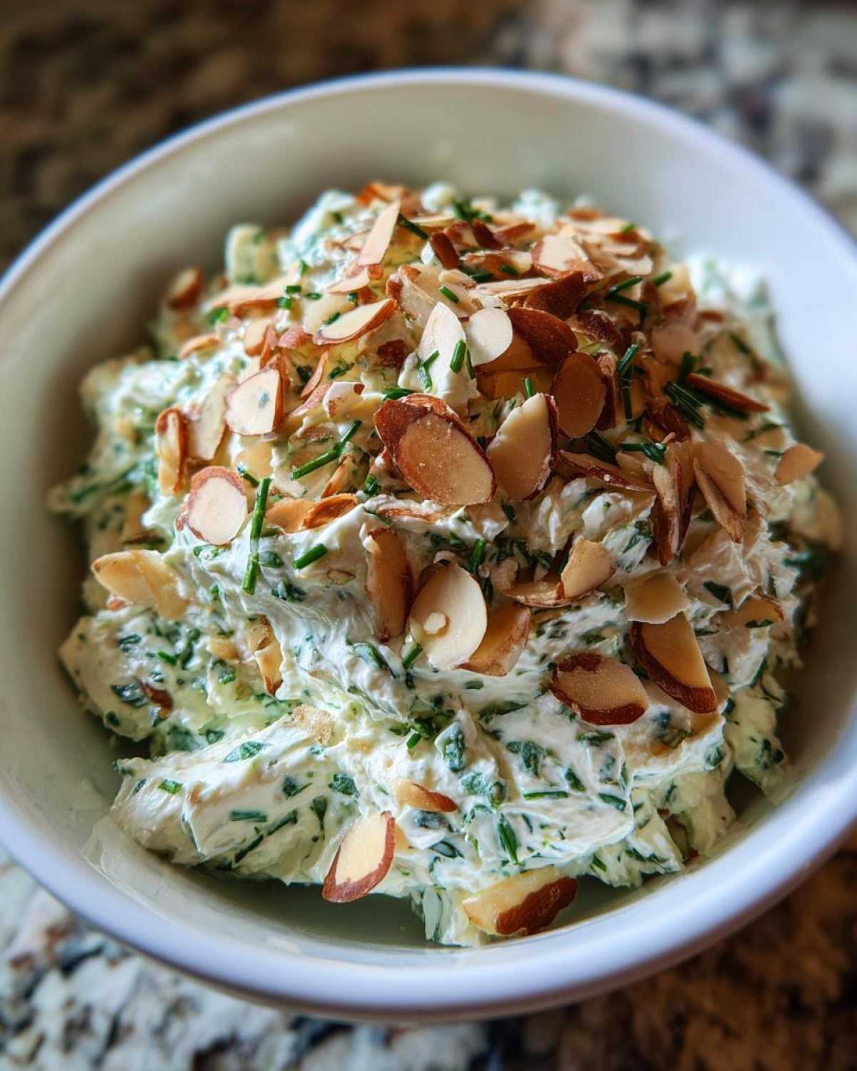 Creamy Chive and Almond Million Dollar Dip topped generously with sliced almonds in a white serving bowl.