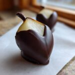 A close-up of a fresh pear half, cut into a heart shape and dipped in dark chocolate, one of the Chocolate Dipped Pear Hearts.