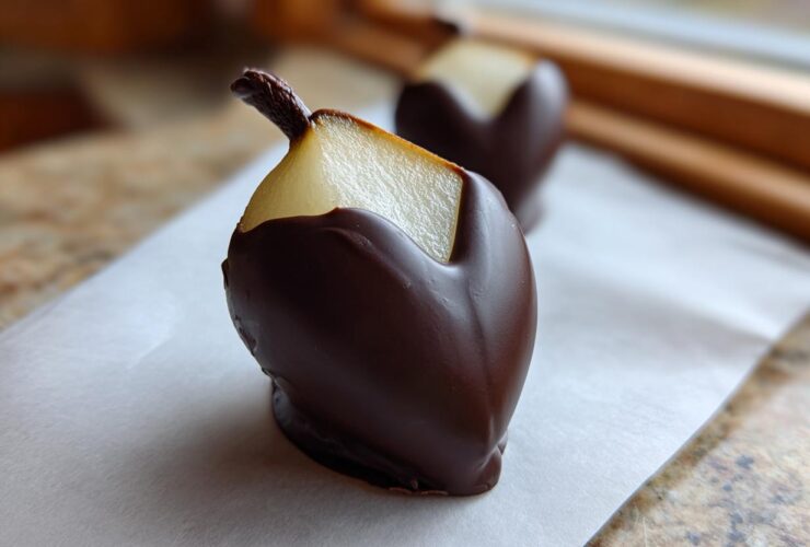 A close-up of a fresh pear half, cut into a heart shape and dipped in dark chocolate, one of the Chocolate Dipped Pear Hearts.