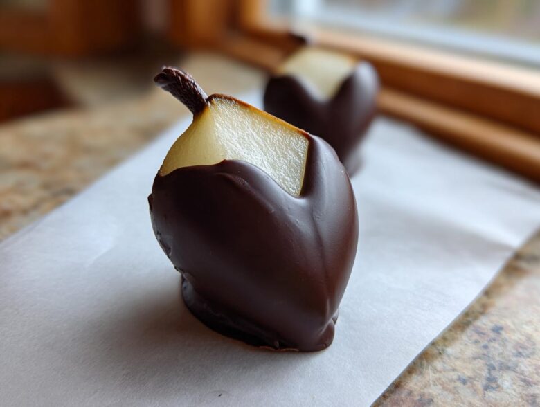 A close-up of a fresh pear half, cut into a heart shape and dipped in dark chocolate, one of the Chocolate Dipped Pear Hearts.