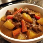 Close-up of a white bowl filled with rich Cowboy Beef Stew with Hearty Vegetables, featuring chunks of beef, potatoes, and carrots.