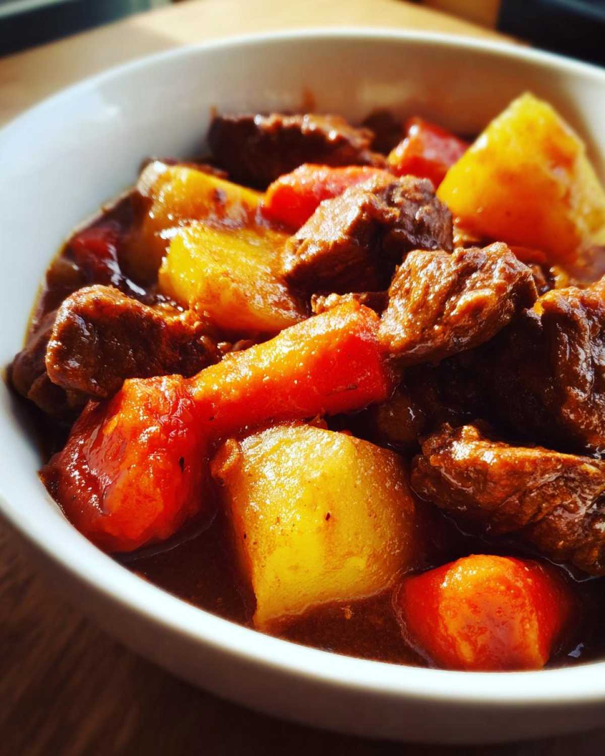 A close-up bowl of rich Cowboy Beef Stew featuring tender chunks of beef, bright orange carrots, and yellow potatoes.