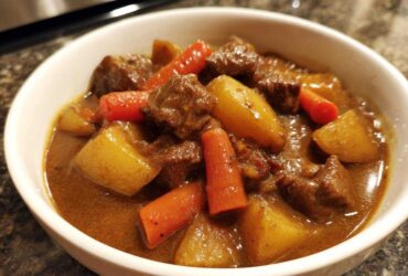 Close-up of a white bowl filled with rich Cowboy Beef Stew with Hearty Vegetables, featuring chunks of beef, potatoes, and carrots.