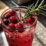 Close-up of a vibrant Cranberry Rosemary Sparkling Spritz garnished with fresh cranberries and a rosemary sprig.