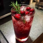 Close-up of a vibrant Cranberry Rosemary Sparkling Spritz garnished with fresh cranberries and rosemary sprigs.