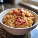 Close-up of creamy lobster risotto served in a white bowl, topped with chunks of bright red lobster meat.