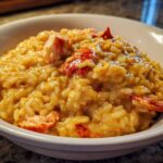 A close-up of rich, creamy lobster risotto served in a white bowl with visible chunks of bright red lobster meat.