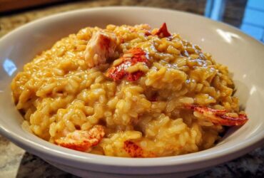 A close-up of rich, creamy lobster risotto served in a white bowl with visible chunks of bright red lobster meat.