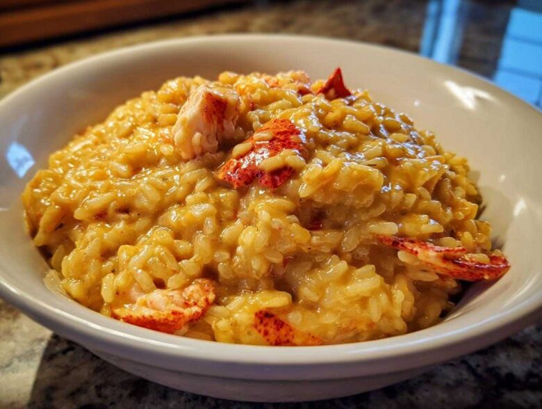 A close-up of rich, creamy lobster risotto served in a white bowl with visible chunks of bright red lobster meat.
