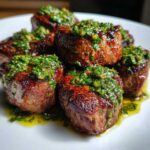 Close-up of seared Filet Mignon Bites topped with vibrant green chimichurri sauce on a white plate.