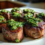 Close-up of seared Filet Mignon Bites topped generously with bright green chimichurri sauce on a white plate.