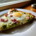 Close-up of a slice of Green Eggs and Ham Breakfast Pizza with a sunny-side-up egg and diced ham.