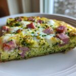 A close-up slice of Green Eggs and Ham Breakfast Pizza featuring green eggs, melted cheese, and diced ham.