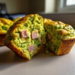 Close-up of a Green Eggs and Ham Savory Muffin cut in half showing green interior and pink ham pieces.