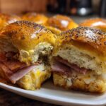 Two freshly baked Ham and Swiss Poppy Seed Sliders on a white plate, showing melted cheese and poppy seed topping.