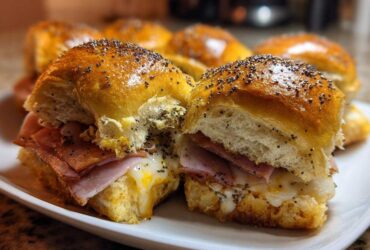 Two freshly baked Ham and Swiss Poppy Seed Sliders on a white plate, showing melted cheese and poppy seed topping.