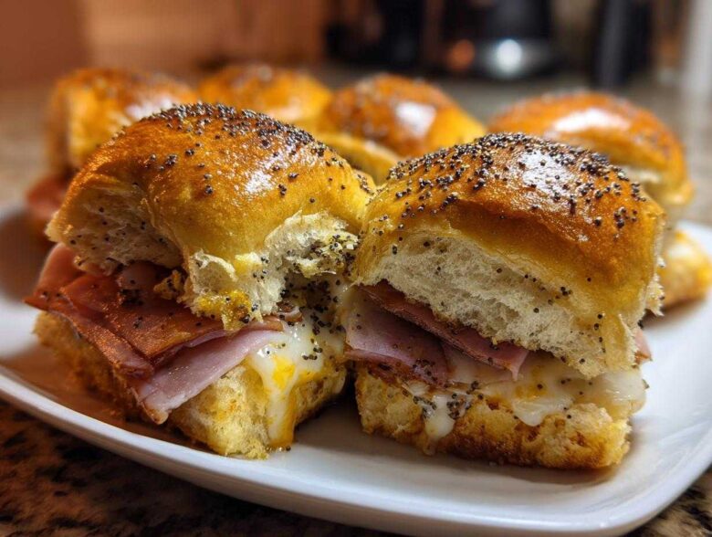 Two freshly baked Ham and Swiss Poppy Seed Sliders on a white plate, showing melted cheese and poppy seed topping.