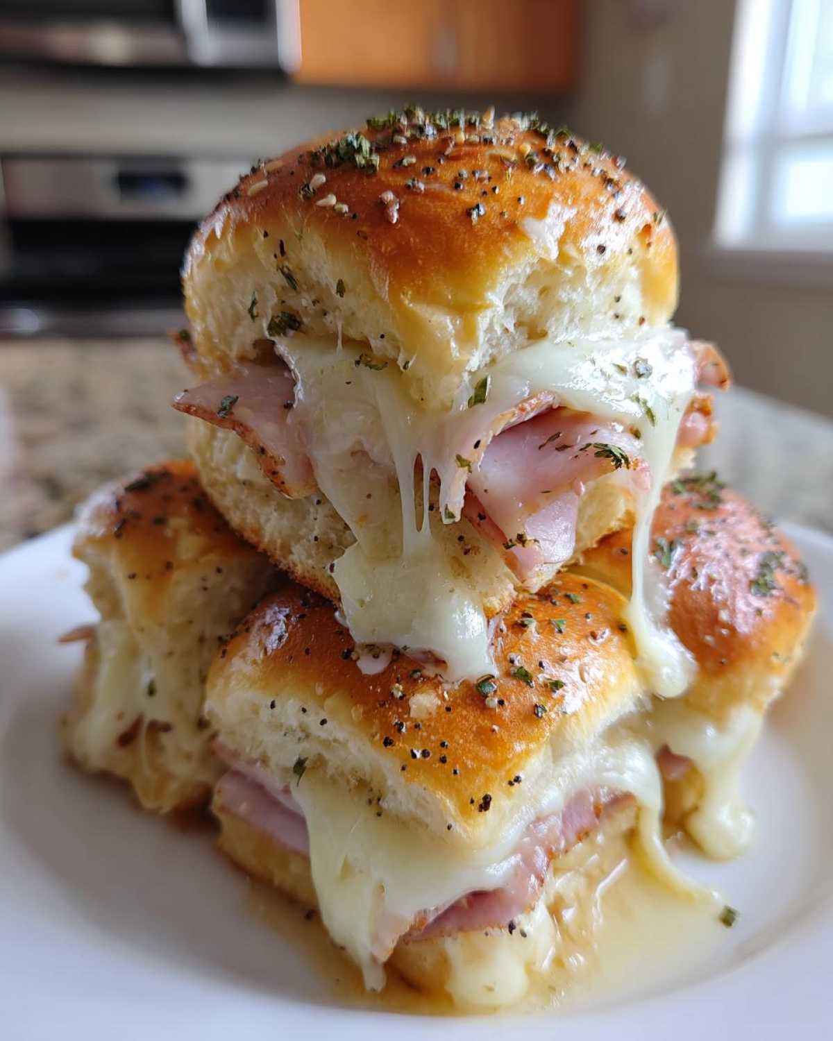 Stack of three Ham and Swiss Poppy Seed Sliders with gooey, melted Swiss cheese dripping down the sides.