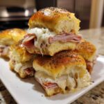 A stack of freshly baked Ham and Swiss Poppy Seed Sliders with gooey melted cheese dripping out.