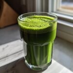 A vibrant glass of Healthy Green Spinach Milkshake with a frothy top, catching sunlight by a window.