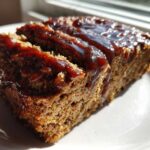 Close-up of a thick slice of moist meatloaf topped with shiny balsamic glaze, ready to eat.