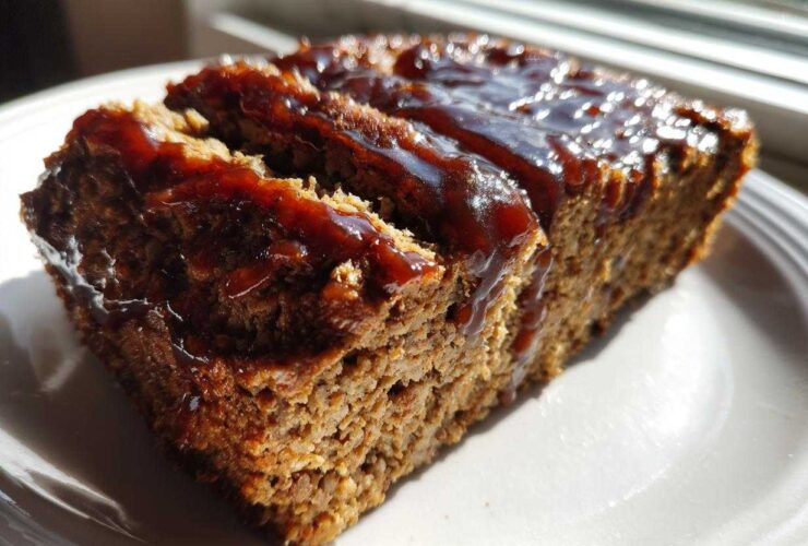 Close-up of a thick slice of moist meatloaf topped with shiny balsamic glaze, ready to eat.