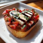 A single piece of Heart-Shaped Tomato & Mozzarella Bruschetta topped with balsamic glaze, served on a white plate.