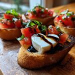 Close-up of Heart-Shaped Tomato & Mozzarella Bruschetta topped with balsamic glaze and basil on a wooden board.