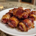 Close-up of several glistening Honey Mustard Bacon Wrapped Smokies piled on a white plate.