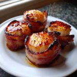 Four perfectly cooked Honey Sriracha Bacon Wrapped Scallops on a white plate with glaze.