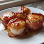 Four perfectly cooked Honey Sriracha Bacon Wrapped Scallops glistening with glaze on a white plate.