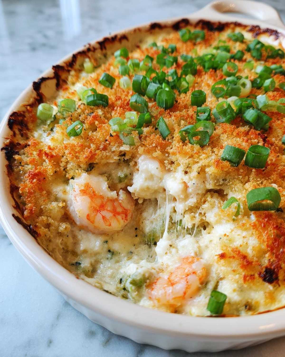 Close-up of a baked Hot Shrimp Jalapeno Popper Dip, showing melted cheese pull, shrimp, and a crispy breadcrumb topping garnished with green onions.