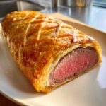 Close-up of an Individual Beef Wellington showing perfectly pink medium-rare tenderloin wrapped in golden, flaky pastry.