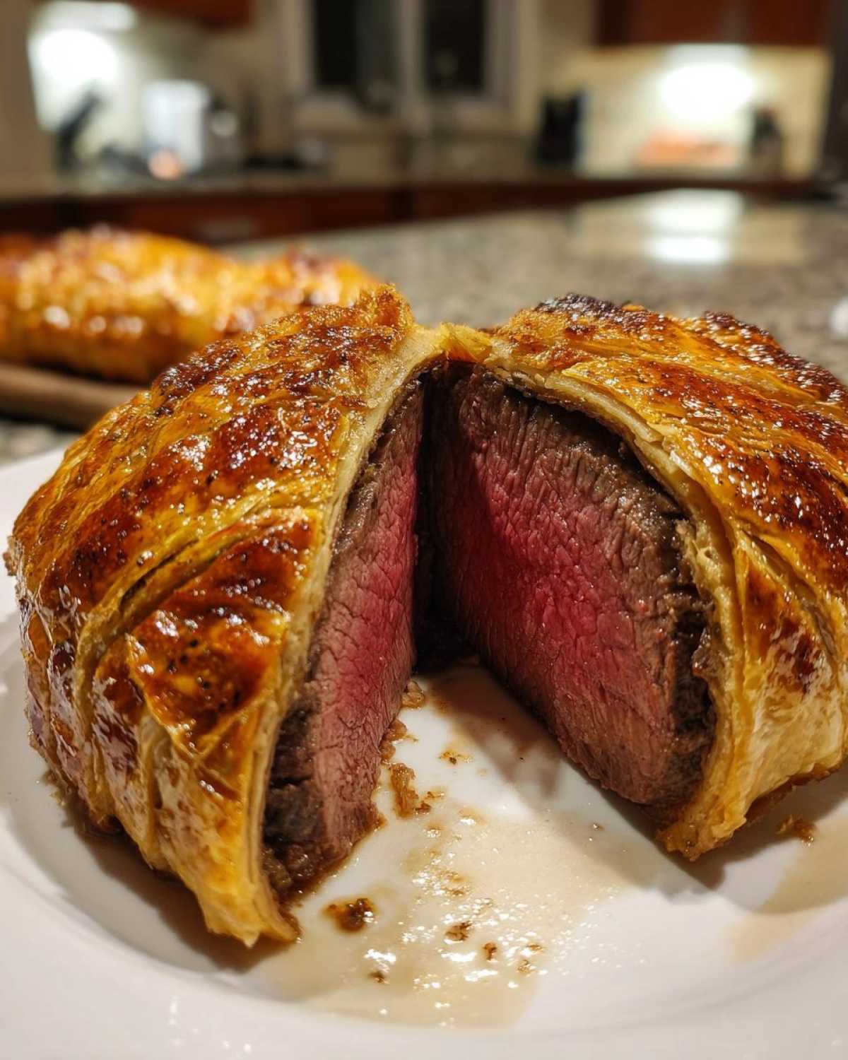 Close-up of an Individual Beef Wellington for Two cut in half, showing medium-rare beef inside golden puff pastry.